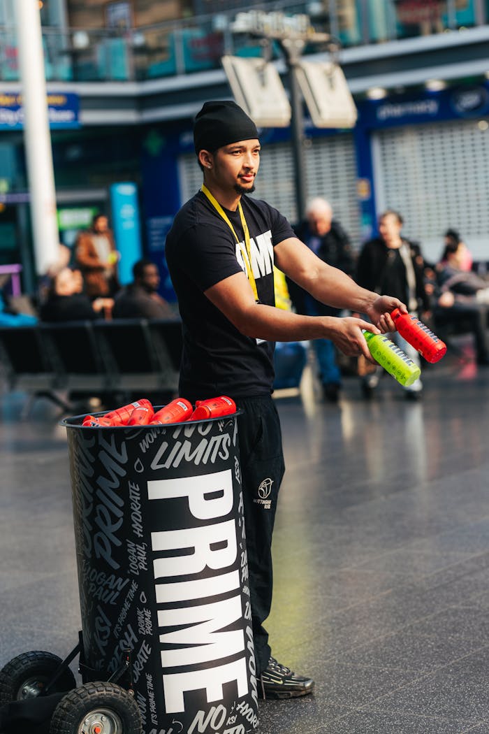 A man presents Prime beverages indoors, engaging the audience at a lively promotional event.