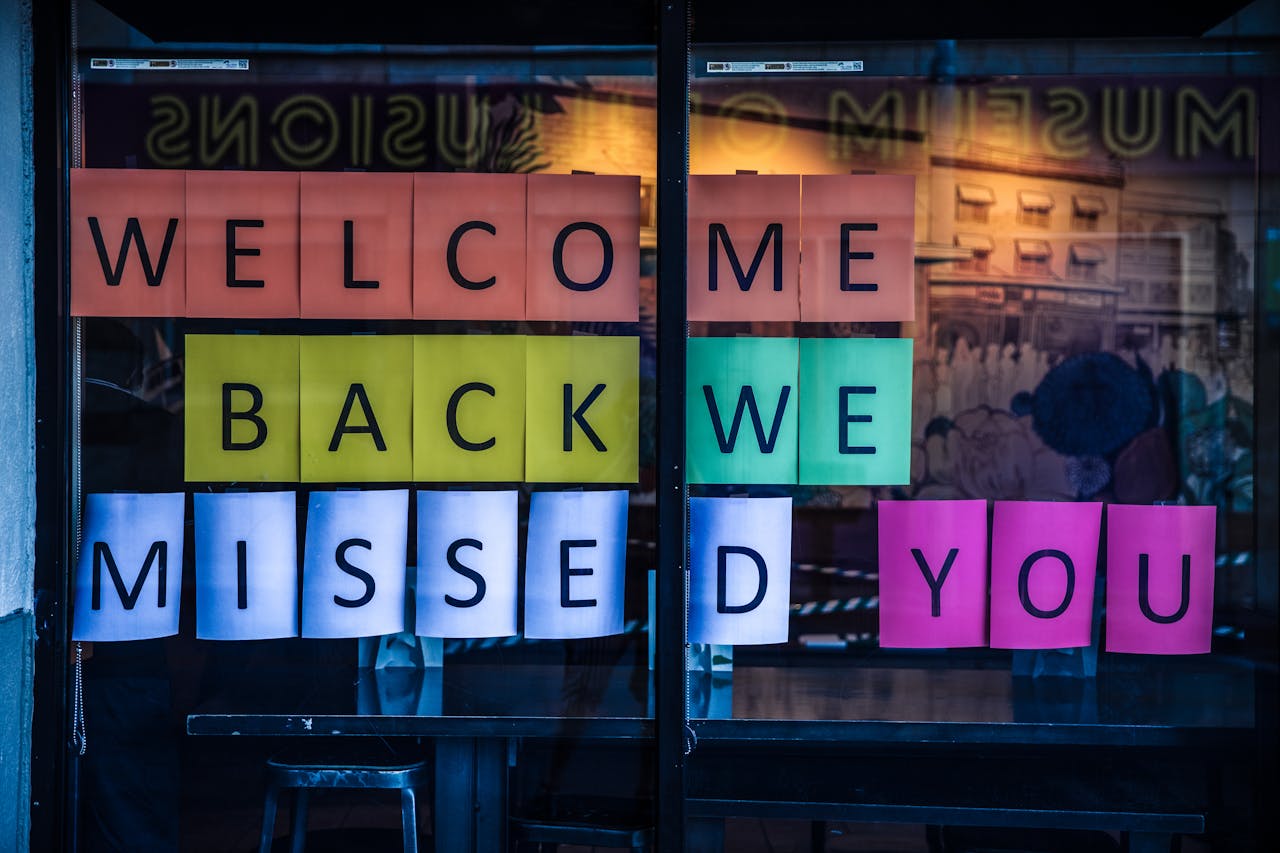 Vibrant sign reading 'Welcome Back We Missed You' displayed on a glass door.